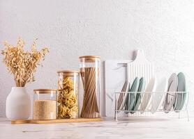 A set of eco-friendly kitchenware, plates in the dryer, glass jars with dry food on a stone countertop. Front view. A copy of the space photo