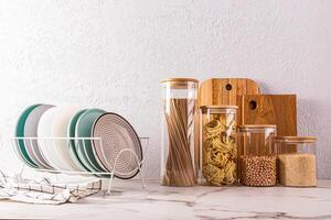 A set of eco-friendly kitchenware, plates in the dryer, glass jars with dry food on a stone countertop. Front view. A copy of the space. photo