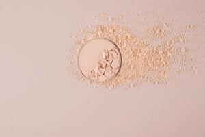 A block of compact powder in a natural tone with the texture of broken pieces stands on a swatch of powder. loose powder. A copy space. top view. photo