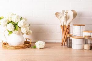 A set of tools for cooking food in a stand, a set of white ceramic jars, a jug with flowering branches in a wooden countertop. Eco style. photo