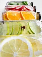 Stacked glass bottles with detox drinks with cucumber, apple, orange, and lemon slices on white background. Vertical orientation, refreshing beverage concept for design and print. photo