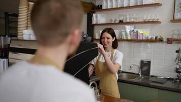 Over the shoulder Happy brunette barista girl in a white T-shirt prepares an order for a male waiter and communicates with him while working in a cafe video