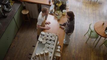 Top view of a brunette girl in a gray sweater makes an order at the counter from the barista of a blond guy in a cafe video