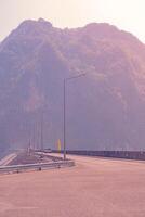 The scene of the road at the top of the dam, with the mountains in the background and a light pole. photo