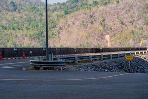 The scene of the road at the top of the dam, with the mountains in the background and a light pole. photo