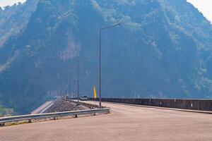 The scene of the road at the top of the dam, with the mountains in the background and a light pole. photo