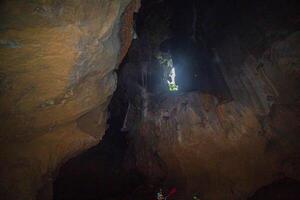 The sun is shining on stalactites and stalmites at the top of the cave. In the cave in Trang, Thailand, there is a small canal. photo