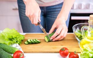 Young woman cuts cucumbers and cooking vegetable salad. Dieting and Healthy eating concept. photo
