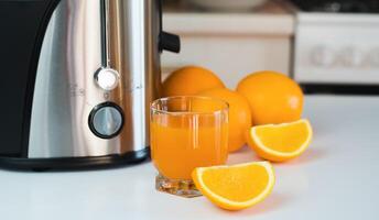 A glass of freshly squeezed orange juice and ripe oranges on the table at the kitchen. Delicious and healthy juices at home. Selective focus. Close-up. photo