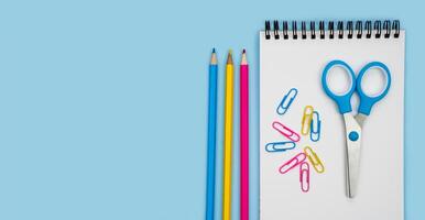 Notebook, scissors and pencils on a blue background. Back to school. Banner. Flatlay. Top view. Copy space. photo