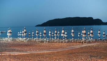 Empty beach with closed beach umbrellas and sunbeds in evening time. Montenegro. Selective focus. photo