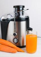 A glass of freshly squeezed carrot juice and a juice extractor on the table in the kitchen. Homemade healthy vitamin juices. Selective focus. Close-up. photo