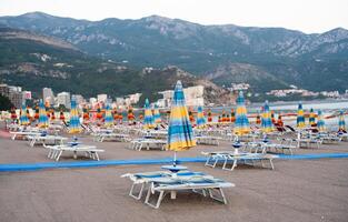 Empty beach with closed beach umbrellas and sunbeds against the backdrop of mountains. Montenegro. Selective focus. photo