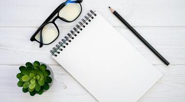 Office desk with blank notepad, glasses and pencil. Mockup notebook. Flatlay composition. Top view. Copy space. photo