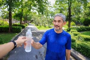 Senior Asian man is drinking water after morning exercise in the park for rehydration of sweat loss and healthy longevity lifestyle concept photo