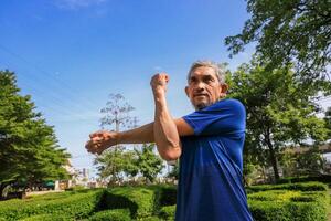 Senior Asian man is stretching his arm and shoulder muscle during warm up exercise work out in the morning at public park for healthy and longevity concept photo