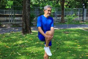 Senior Asian man is stretching his leg muscle during warm up exercise work out in the morning at public park for healthy and longevity photo