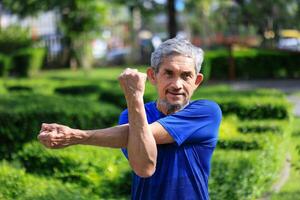 Senior Asian man is stretching his arm and shoulder muscle during warm up exercise work out in the morning at public park for healthy and longevity concept photo