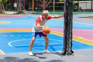 Senior Asian man in retirement age is playing basketball at outdoor court for healthy and fun activity to exercise and workout against aging illness photo