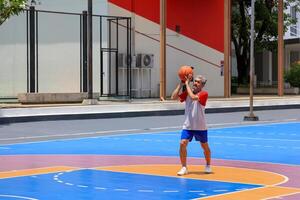 Senior Asian man in retirement age is playing basketball at outdoor court for healthy and fun activity to exercise and workout against aging illness photo