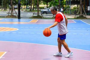 Senior Asian man in retirement age is playing basketball at outdoor court for healthy and fun activity to exercise and workout against aging illness photo