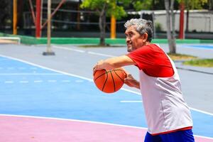 Senior Asian man in retirement age is playing basketball at outdoor court for healthy and fun activity to exercise and workout against aging illness photo