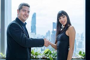 Caucasian businessman is shaking hand with his partner while working in modern working space with the view of business downtown and skyscraper photo