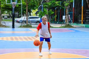 Senior Asian man in retirement age is playing basketball at outdoor court for healthy and fun activity to exercise and workout against aging illness photo
