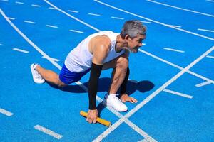 Senior Asian athlete is practicing running block start in the professional blue track for professional exercise, sport training workout and healthy for longevity photo