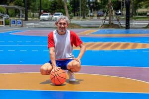 Portrait of senior Asian man in retirement age is playing basketball at outdoor court for healthy and fun activity to exercise and workout against aging illness photo
