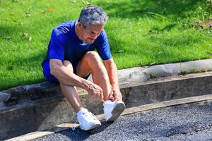 Senior Asian man is tying knot on his running trainer in the morning jogging exercise for healthy and work out concept photo