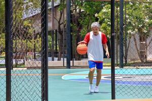 Senior Asian man in retirement age is playing basketball at outdoor court for healthy and fun activity to exercise and workout against aging illness photo