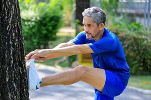 Senior Asian man is stretching his leg muscle during warm up exercise work out in the morning at public park for healthy and longevity photo