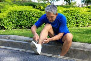 Senior Asian man is tying knot on his running trainer in the morning jogging exercise for healthy and work out photo
