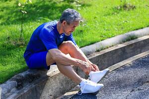 Senior Asian man is tying knot on his running trainer in the morning jogging exercise for healthy and work out photo