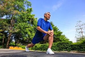 Senior Asian man is stretching his leg muscle during warm up exercise work out in the morning at public park for healthy and longevity photo