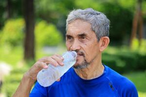 Senior Asian man is drinking water after morning exercise in the park for rehydration of sweat loss and healthy longevity lifestyle photo