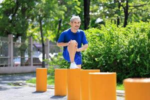Senior Asian man is stretching his leg muscle during warm up exercise work out in the morning at public park for healthy and longevity concept photo