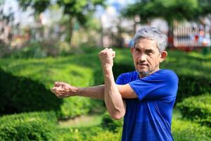 Senior Asian man is stretching his arm and shoulder muscle during warm up exercise work out in the morning at public park for healthy and longevity photo