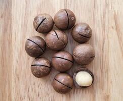collection of macadamia nuts arranged on a wooden surface. One of the nuts is partially cracked open, revealing the white kernel inside photo