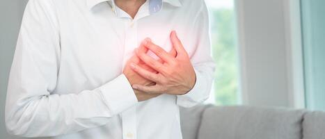 hand hold chest with heart attack symptoms, asian man working hard have chest pain caused by heart disease, leak, dilatation, enlarged coronary heart, press on the chest with a painful expression photo