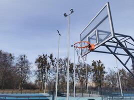 A basketball net under a cloudy sky. The back board has been busted and is now covered with a large piece of wood. photo