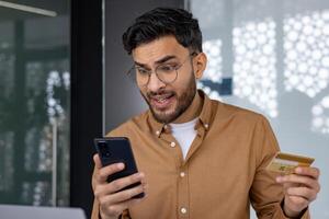 Man experiencing frustration while checking credit card transaction on smartphone. Concept of online shopping, financial problem, or fraud. photo