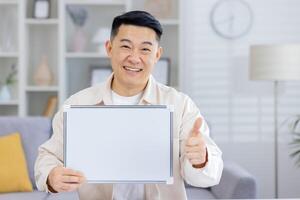 Cheerful man presenting a blank whiteboard and showing a thumbs up gesture while standing in a bright, modern living room setting photo