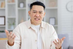 Frustrated man displaying emotions of anger and dissatisfaction at home, gesturing with raised hands. photo
