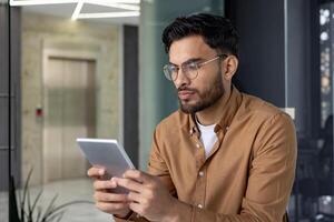 Man using a tablet with serious expression in a modern, well-lit office. Captures concentration, technology, and professional settings. photo