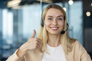 Friendly female customer service representative showing a thumbs up gesture, smiling with a headset on in a contemporary office. photo