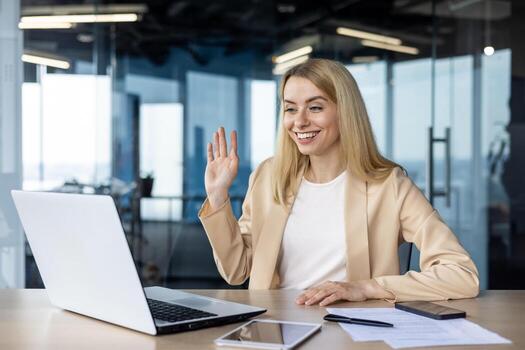 un profesional mujer sonriente y ondulación en un moderno oficina configuración, comprometido en un llamada en su ordenador portátil. brillantemente iluminado habitación mejora el positivo y acogedor atmósfera. foto