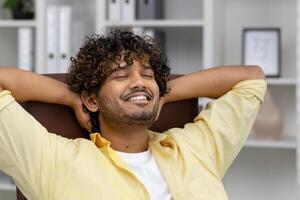 Man sitting at a desk with closed eyes and a relaxed smile, enjoying a moment of calm and peace. photo