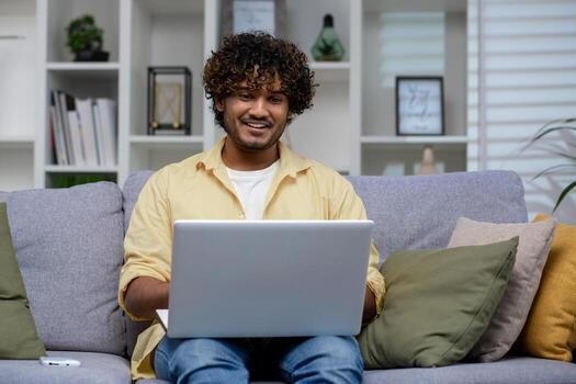 un relajado hombre en casual atuendo trabajos en un ordenador portátil mientras sentado en un acogedor sofá, exudando un sentido de comodidad y productividad a hogar. foto